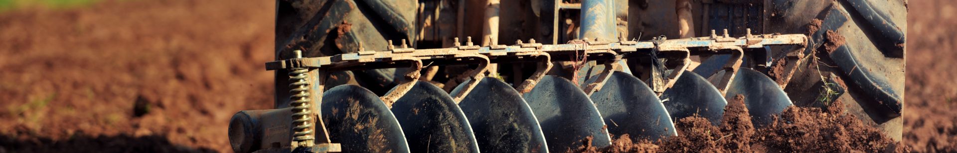 A tractor plows a field with a disc harrow, turning over soil under a clear sky